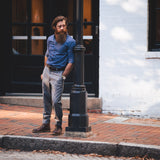 Man in city, leaning against a light pole in a blue Savage Gentleman dress shirt.