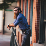 Man leaning against railing wearing blue dress shirt.