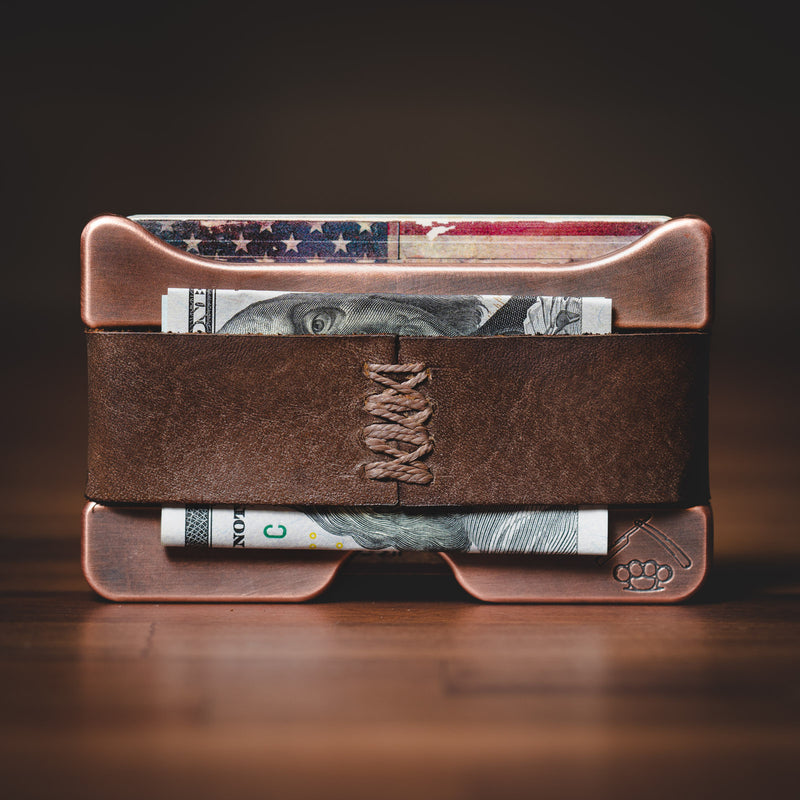 Savage Gentleman copper wallet holding cash underneath it's brown leather strap.