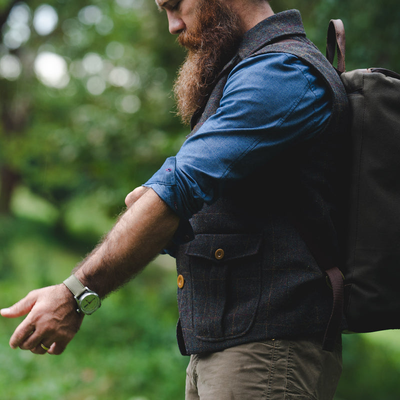 Man rolls sleeves while hiking in the woods with a backpack.