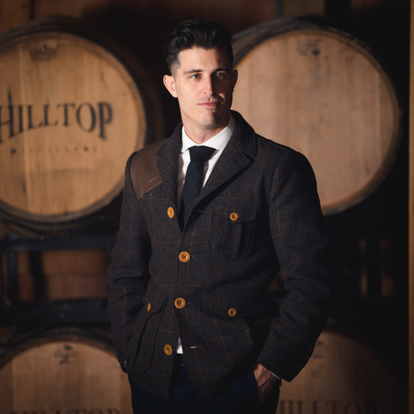 Man wearing sporting jacket in front of whiskey barrels. 