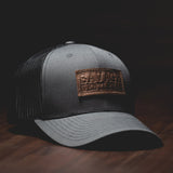 Savage Gentleman Leather Patch Trucker Hat in black mesh and charcoal.